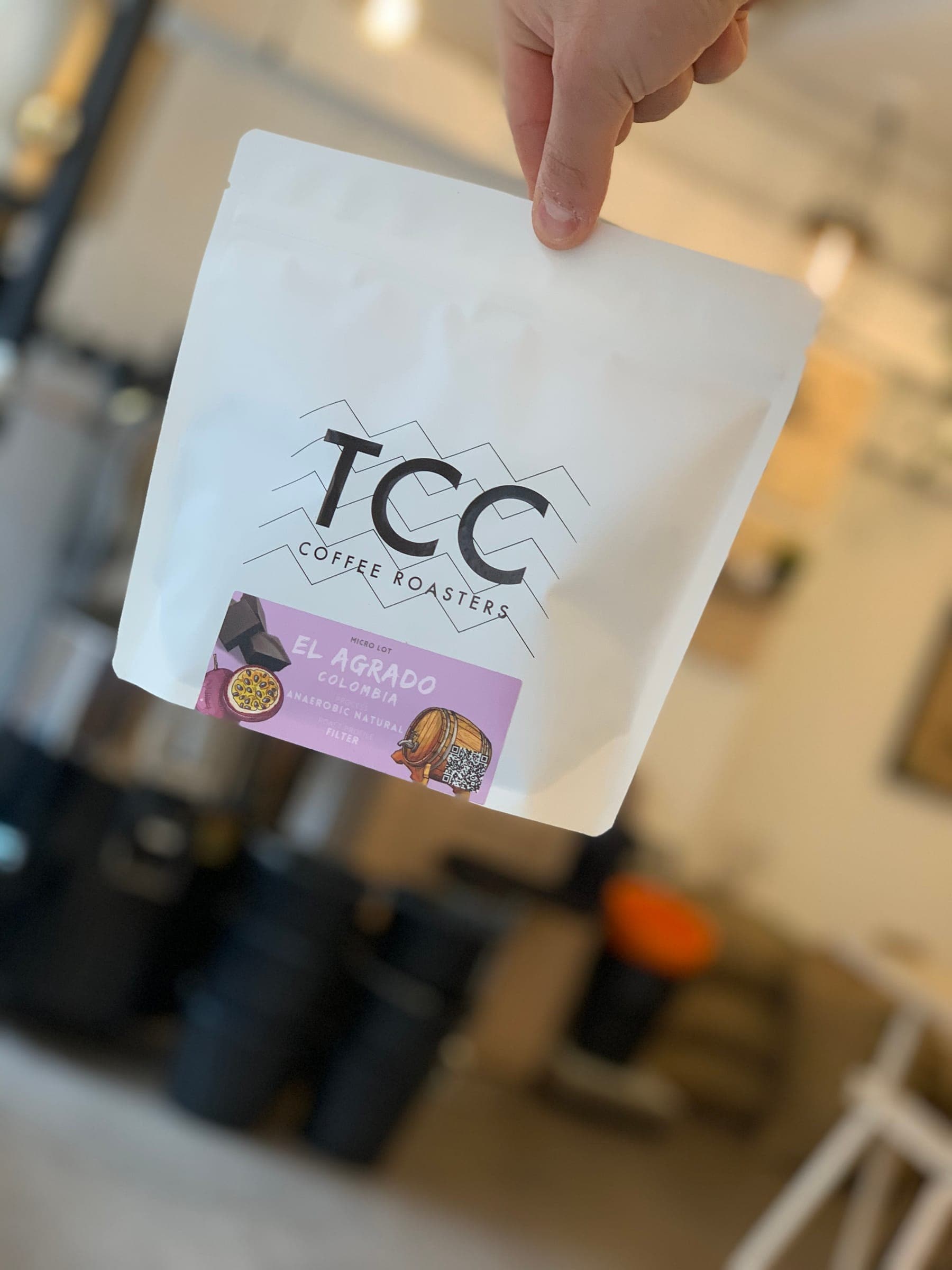 A hand holding a freshly roasted bag of TCC coffee at the roastery