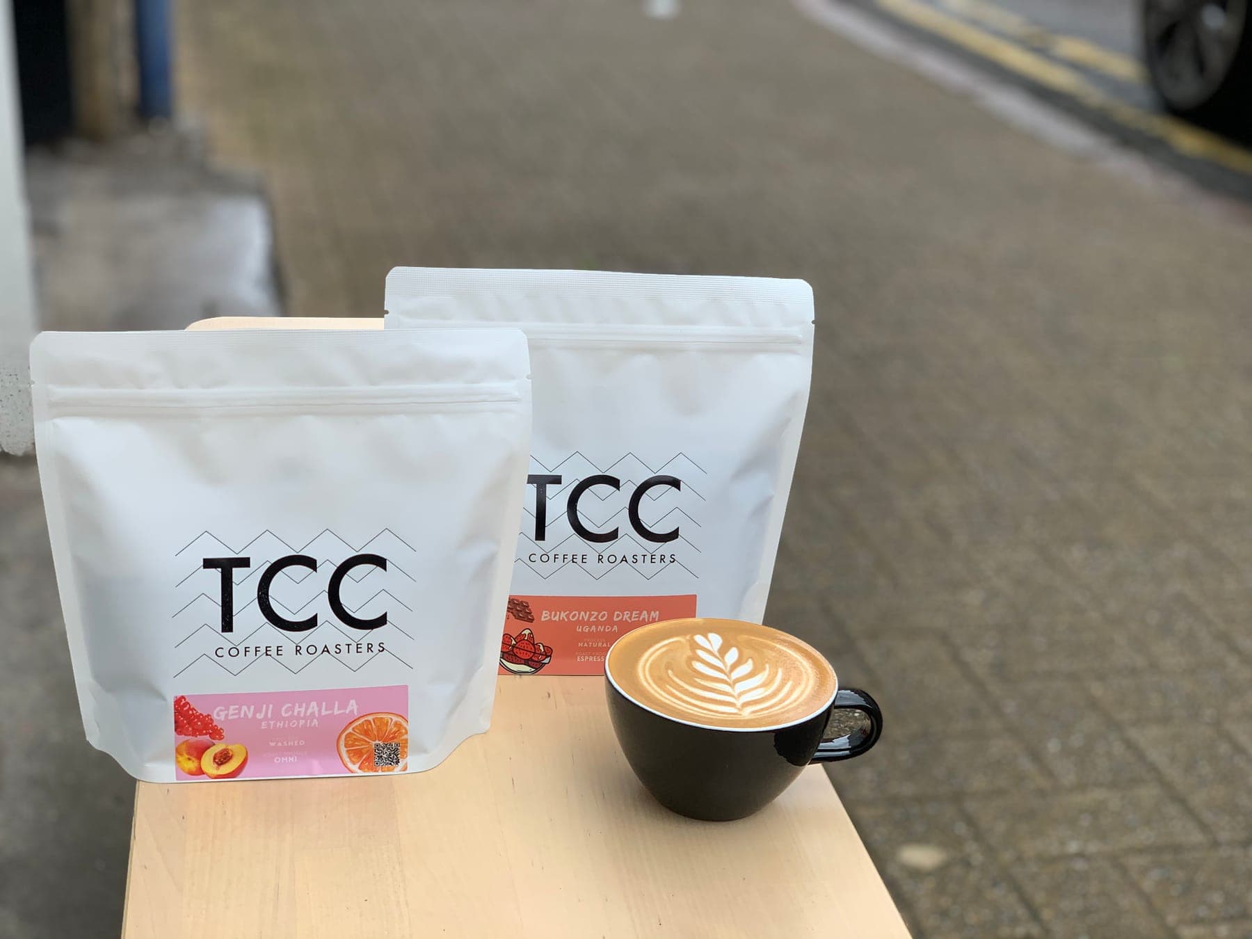 TCC coffee bags beside a flat white with latte art
